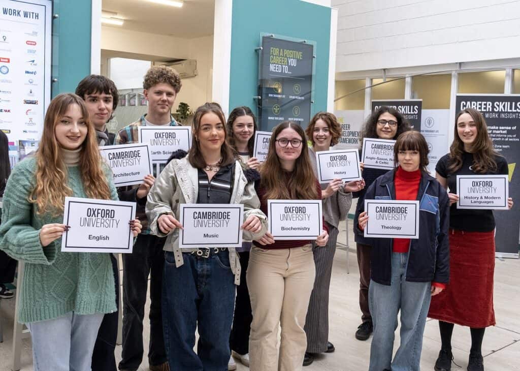 Smiling students holding cards displaying the name of the university they are attending and the subjects they will study. 