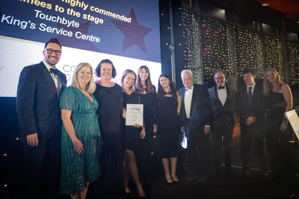 Eight members of staff from Hiyield collect the SME Employer of the Year award on stage with presenters Holly Day and Neil Caddy at either end of the group.