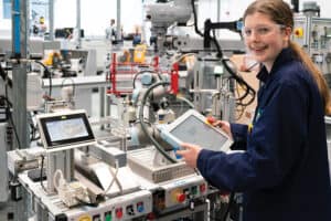 an engineering student is stood in front of a machine smiing