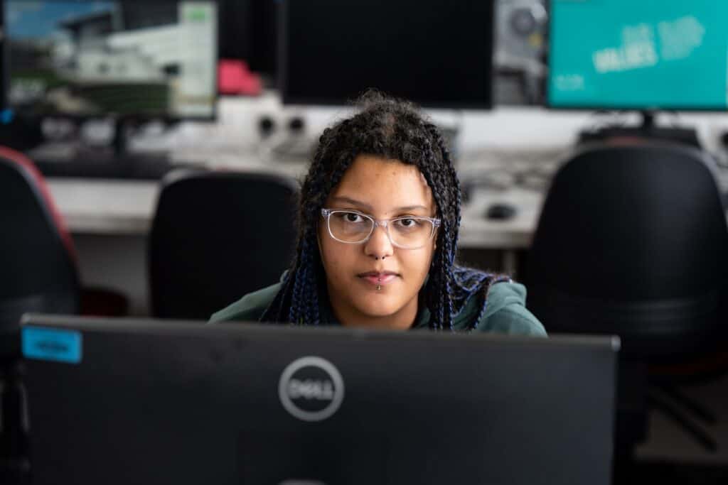 A student with braids looks over their computer screen towards the camera.