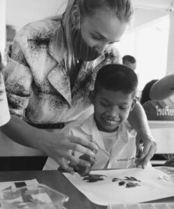 Young woman with face mask helps a child in hand painting