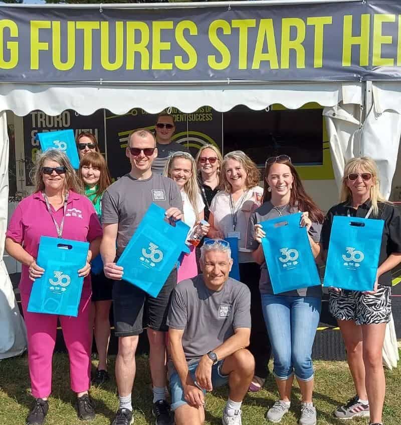 The Truro and Penwith College team at Royal Cornwall Show in 2023. They are all smiling in front of their stand and holding blue goodie bags.