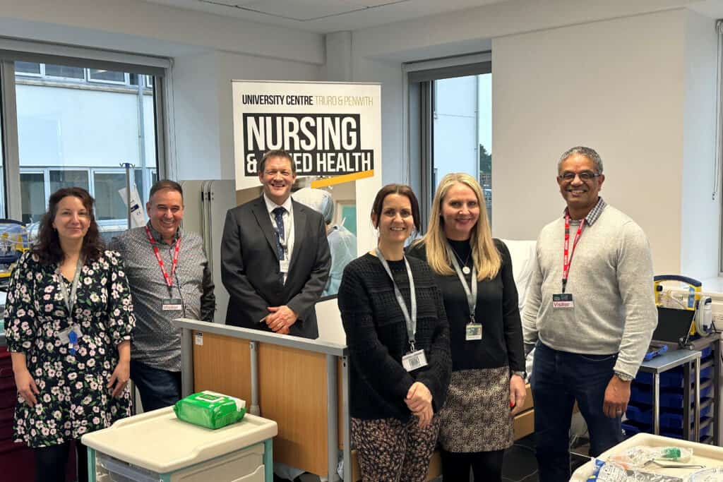 A group photo of senior members of staff from Truro College with external visitors. There is a banner for Nursing and Allied Health behind them.