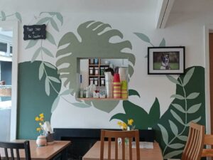 An image of the inside of a cafe. There are brown dining tables and the walls are painted with leaves.