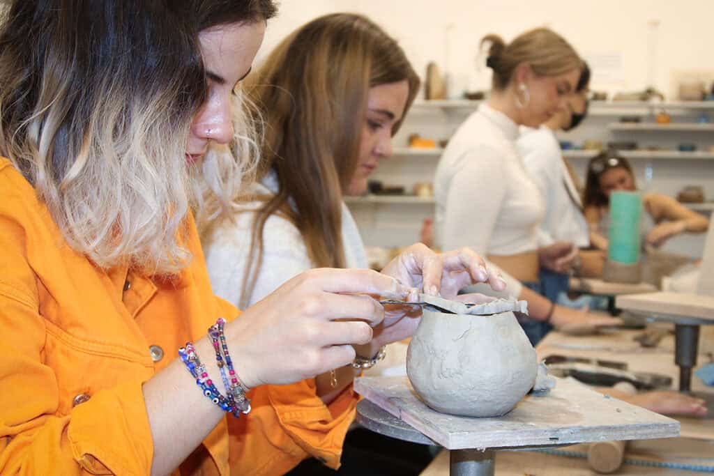 A close up of students who are sculpting clay pots in an art studio.