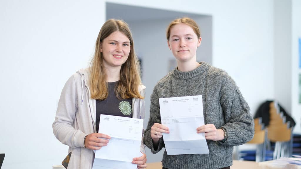 Two students standing together whilst holding their A Level results.