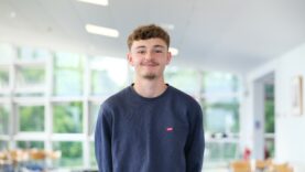 Young man in blue jumper smiles at the camera.
