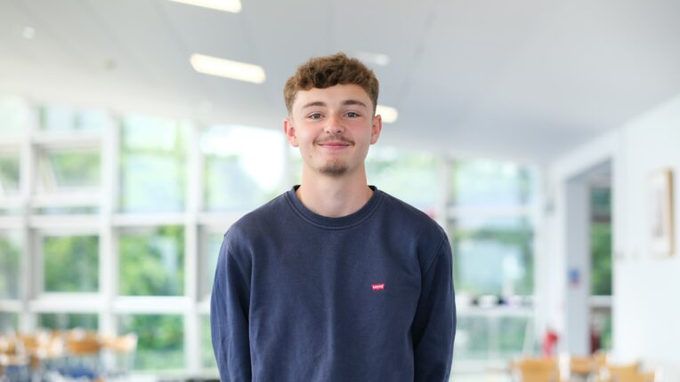 Young man in blue jumper smiles at the camera.