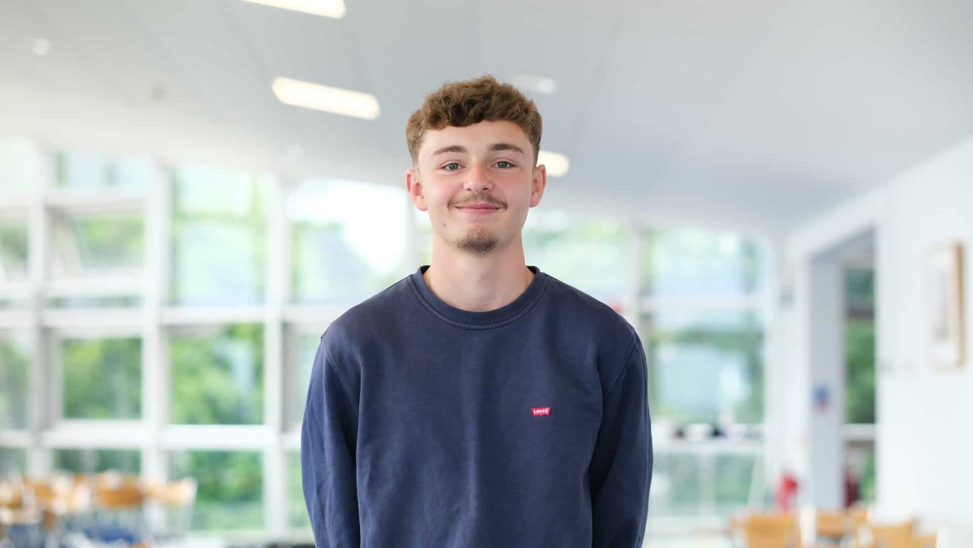 Young man in blue jumper smiles at the camera.