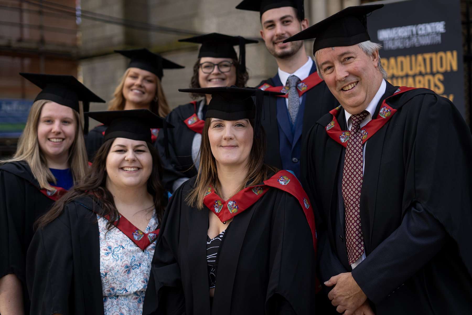 A group of students in Graduation robes pose together on the steps of Truro Cathedral at the University Centre Truro & Penwith Graduation.