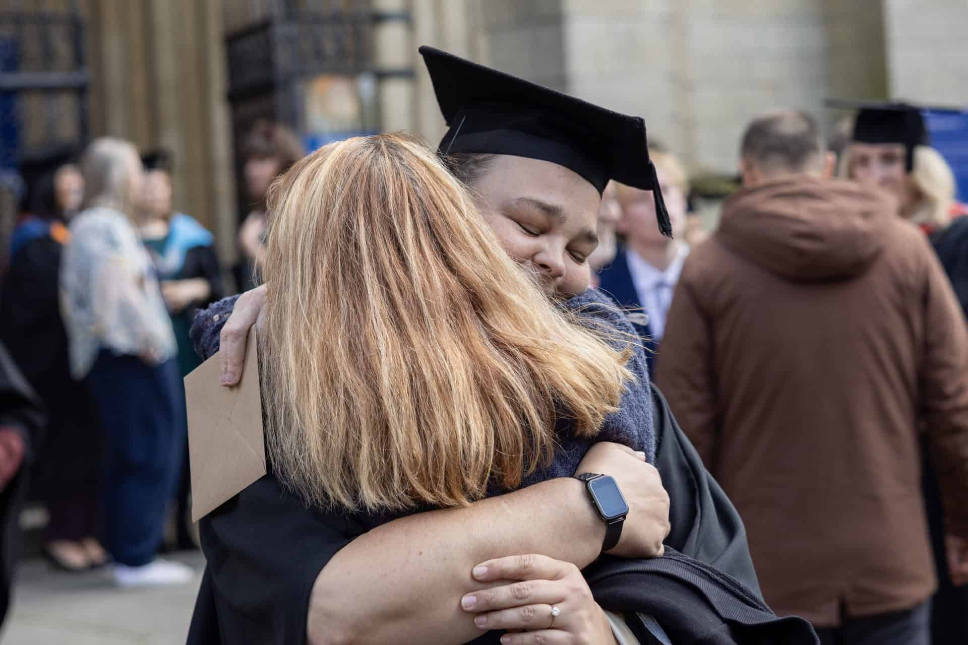 Graduation 24 06 A student dressed in Graduation robes hugs another unknown person tightly outside Truro Cathedral.