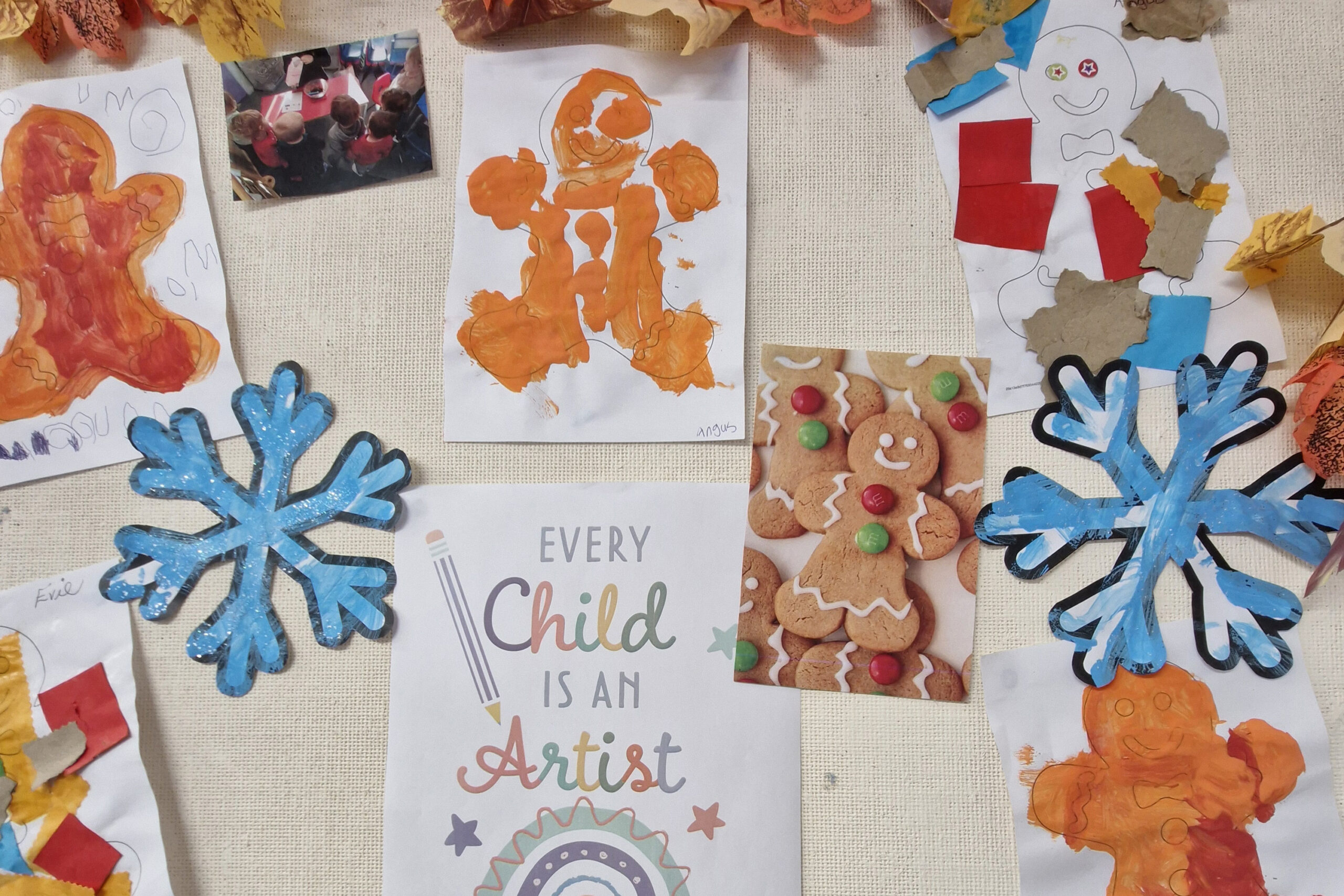Pictures of gingerbread men which have been painted by children are on a noticeboard. There are also a couple of photos, two snowflakes that have been painted and a sign which says 'every child is an artist'.