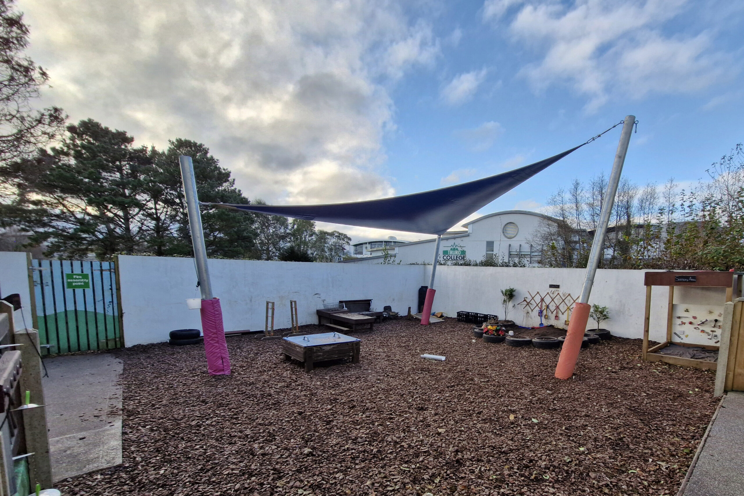 An image of the outside play area at Truro College's Nursery. There is a structure that provides cover, a sensory area and a digging pit.