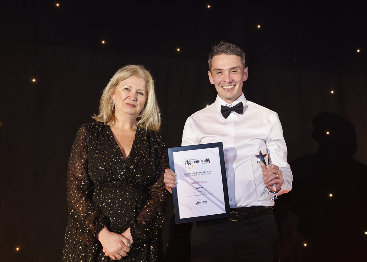 Tom Heap smiles down camera with his certificate and trophy aloft. to his left is Cathie Kessell from Cornwall Opportunities, category sponsors