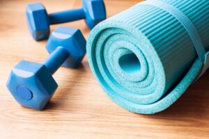 A close up image of a pair of blue dumbells and a blue yoga mat.