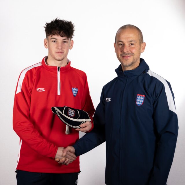 Two people dressed in football kit shake hands and pose for the camera.