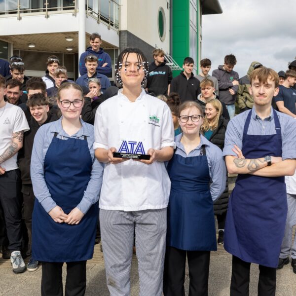 A group of apprentices stand outside a college building holding an award.