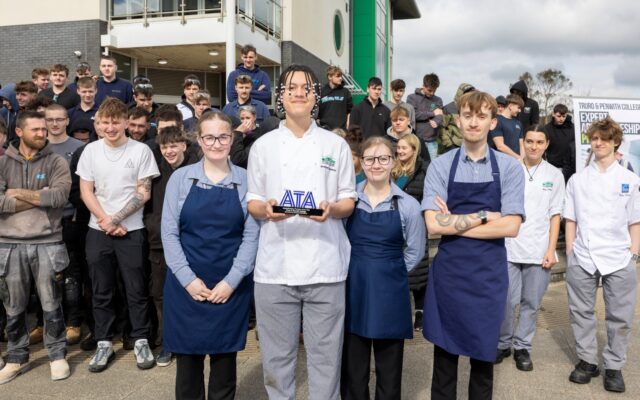 A group of apprentices stand outside a college building holding an award.