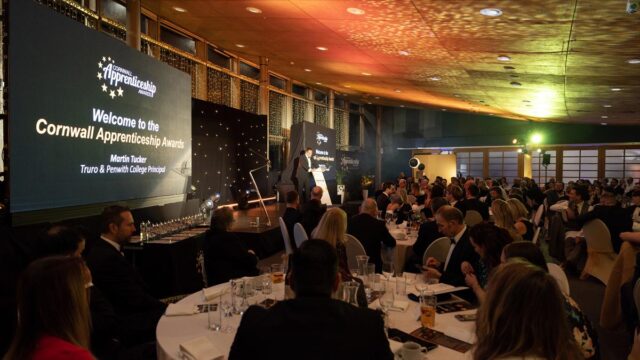 A shot of the room and stage set with two huge screens as the College Principal Martin Tucker opens the event.