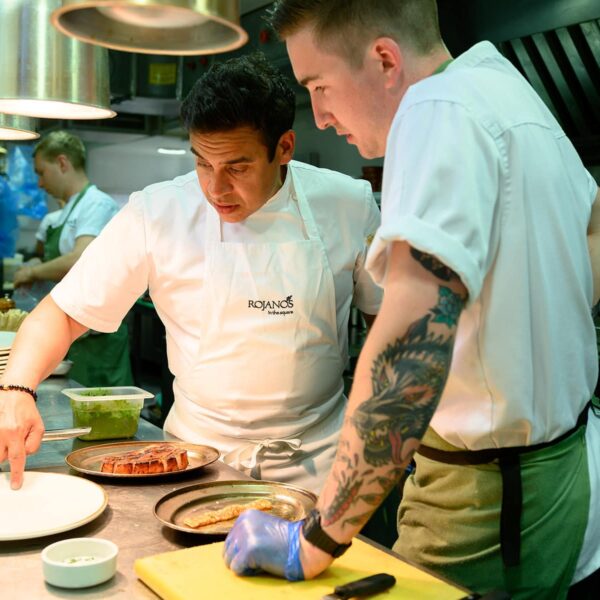 Chef Paul Ainsworth is with another chef and they are both looking at two dished under heat lamps.