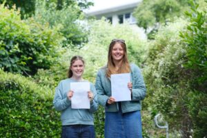 Bella and Laurn smile down camera holding their results in a nice green area of the college.