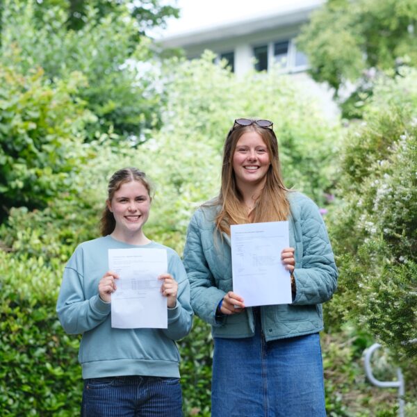 Bella and Lauren stand surrounded by greenery and hold their results in front of them.