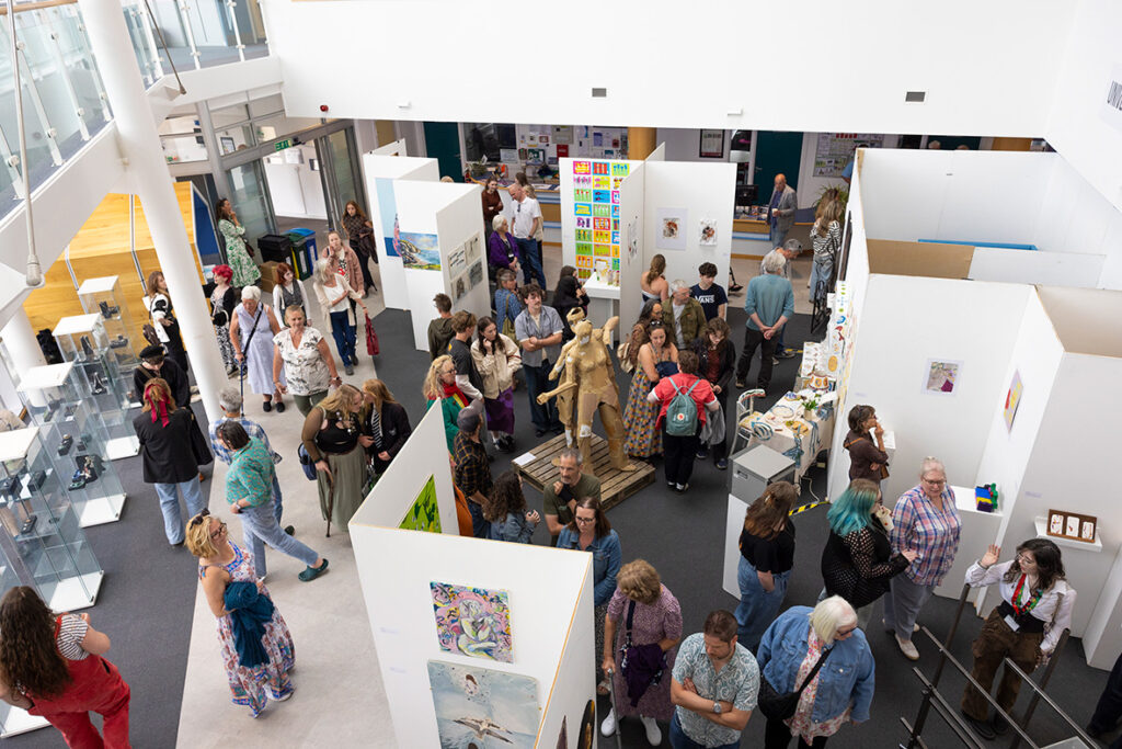 Large displays of student artwork is set up in the Fal buidling. Lots of guests are moving around the artwork on display.