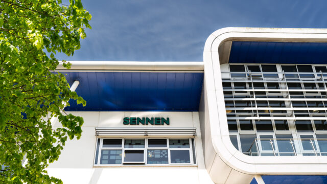 A photo of the outside of the Sennen building. You can see the building name, a part of a tree and the blue sky.