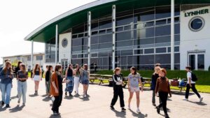 Students walking in front of the Lynher building at Truro College. There are picnic benches and grass