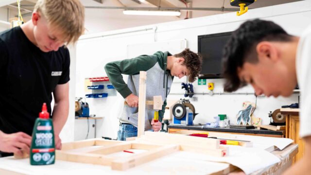 Three students are working with wood and tools in the College's construction area.