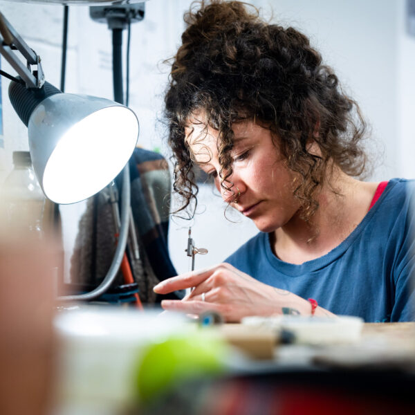 A woman works on a piece of jewellery in a silversmithing studio.