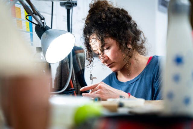 A woman works on a piece of jewellery in a silversmithing studio.