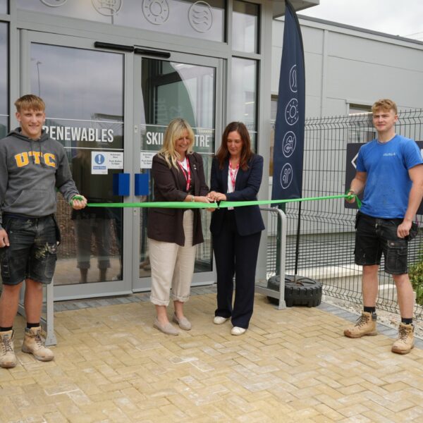 Two students hold out a green ribbon while two other people cut the ribbon with a pair of scissors.