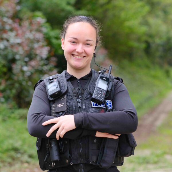 A female police officer stands with her arms folded, smiling at the camera.