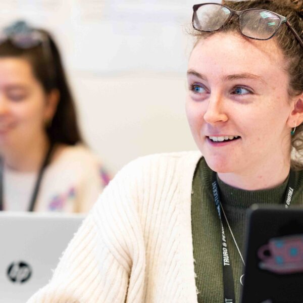 A close up of a student who has a laptop open in front of her. She wears a lanyard and has glasses on top of her head.