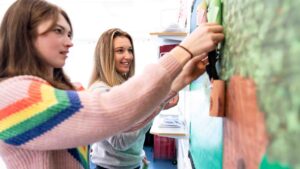 Two students pin child creations to a noticeboard