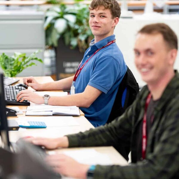 An apprentice from the Eden Project sits at a computer and another person sits to the side.