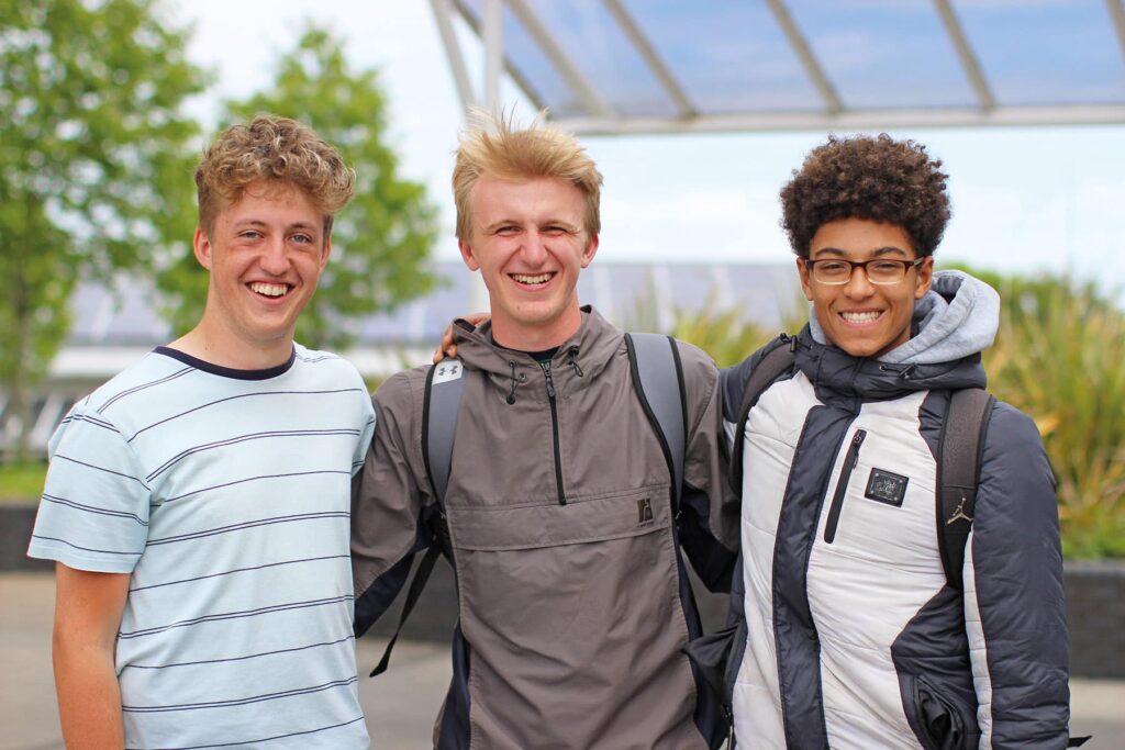 Three students with their arms around each other smile at the camera.