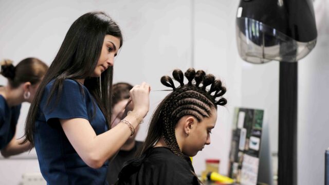 A hair and beauty student is styling the hair of a young person sat in a chair in front of her.