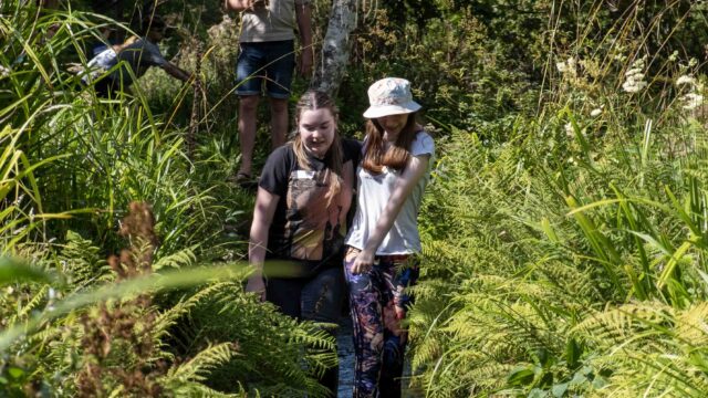 Two students take part in the IB Diploma induction day. They are joined together by an ankle and they are walking their way down a stream.