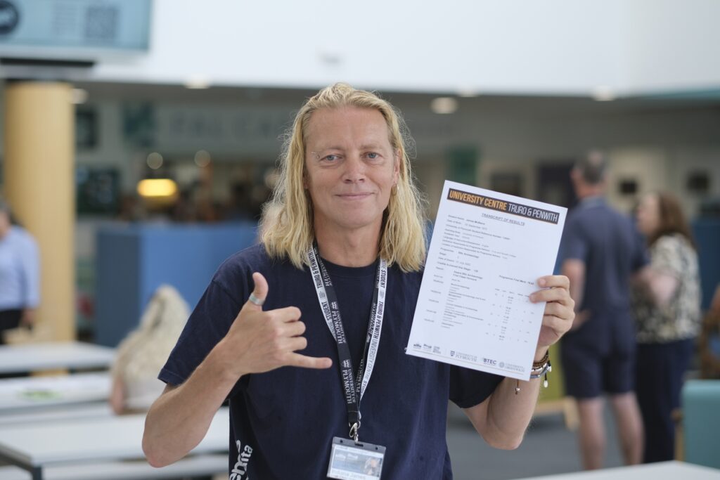 James McBlane holds his results and smiles down camera while giving a thumbs-up