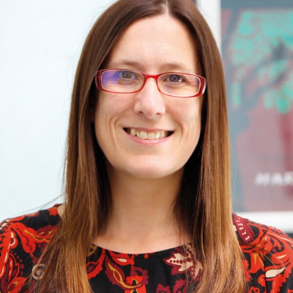 A photo of Jennifer McConnell who is wearing a red dress, red glasses and brown hair.
