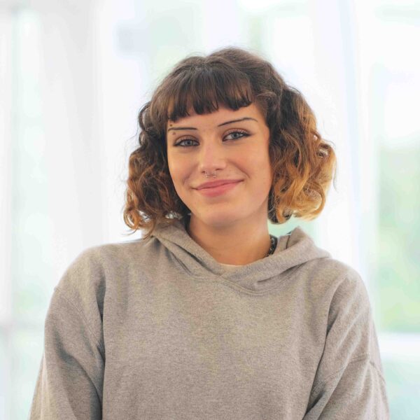 Student, Jessie, smiles at the camera. She is wearing a grey hoodie and has short curly hair.