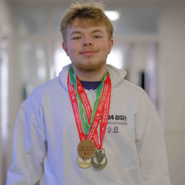 Student Logan stands in a hallway wearing a white hoodie and wearing multiple medals around his neck.