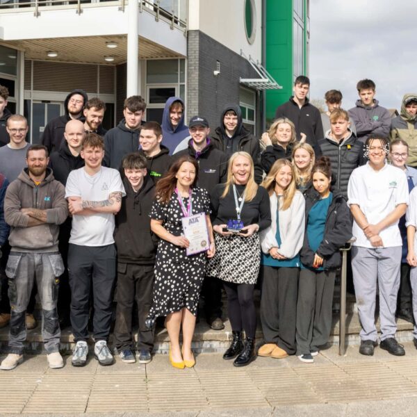 Apprentices and staff gather outside the college holding a trophy and certificate.