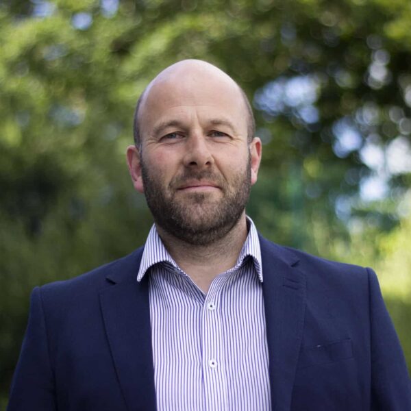 Mark Lewin is wearing a stripe shirt and a navy suit jacket.