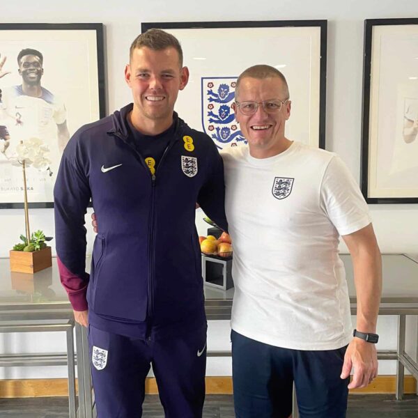 Two people in football kit smile and put their arms around each other.