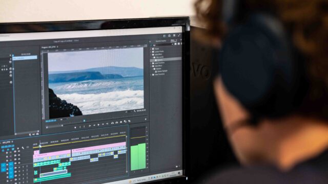 The camera looks over the shoulder of a student who is editing a video of the sea on a computer.