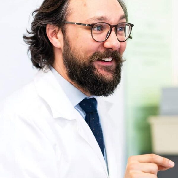 A photo of Ned Crowley, Head of Faculty for Science. He is wearing a lab coat, a shirt and tie and glasses.