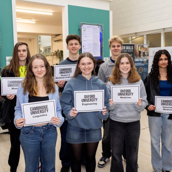 A group of students stand holding bits of paper that says which University they are attending and what they are studying.